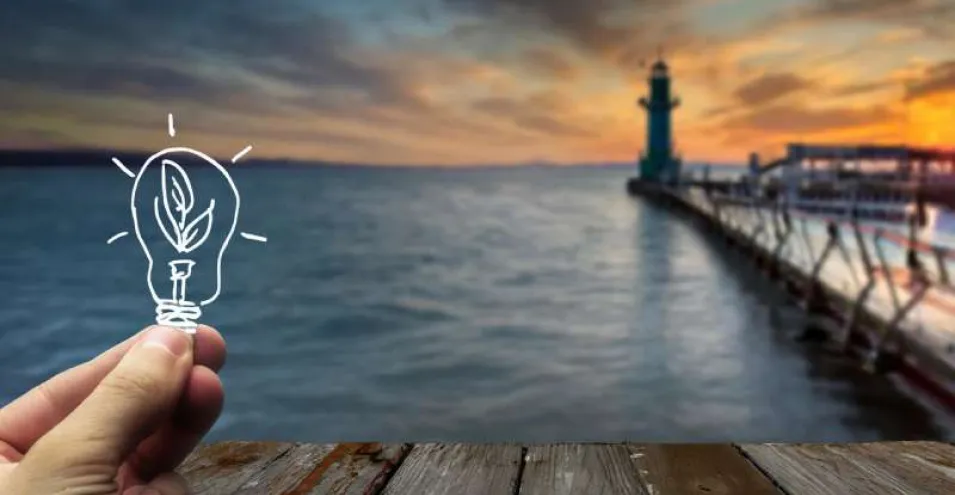 Faro con puesta de sol y mano sujetando bombilla dibujada